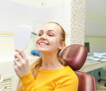 Lady checking teeth in mirror. Young female at dentist office.